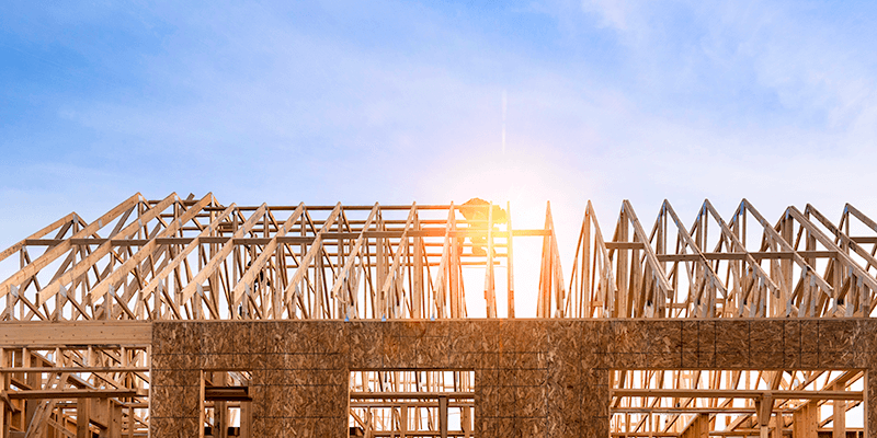 Wooden roof truss and frame. Home under construction. Sun shining through framing, blue sky with wispy clouds. 