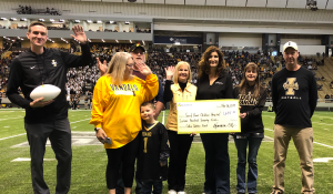 Group of eight people standing in a football field with a big check being held up by the middle three people.
